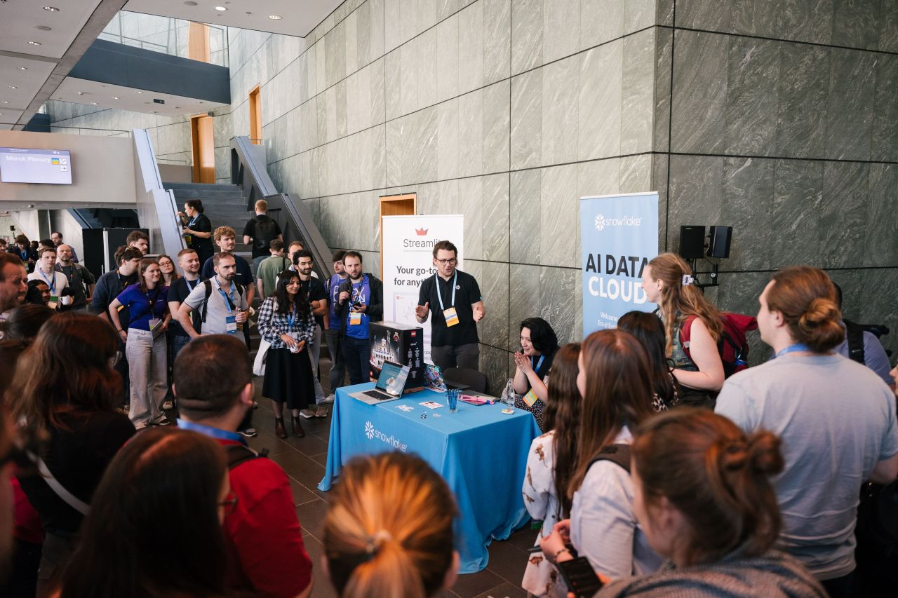 A crowd of attendees gathered around a sponsor booth in the venue foyer